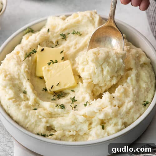 Luxurious Garlic Mashed Potatoes 7 Mashed potatoes in a bowl with melted butter and fresh thyme.