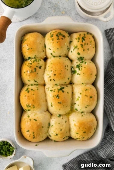 Freshly baked cheesy garlic rolls in a baking dish being brushed with melted butter and parsley.
