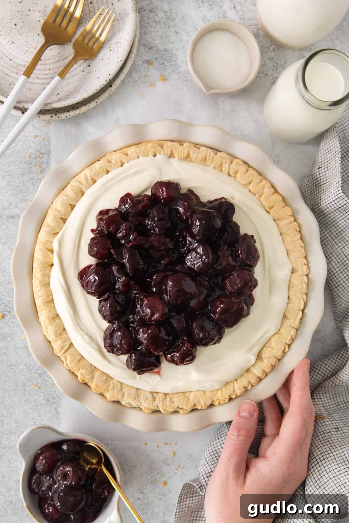 Dreamy Cherry Cream Cheese Pie 6 A person gently holding a cherry cream cheese pie, poised to serve a slice, with a beautiful table setting in the background.