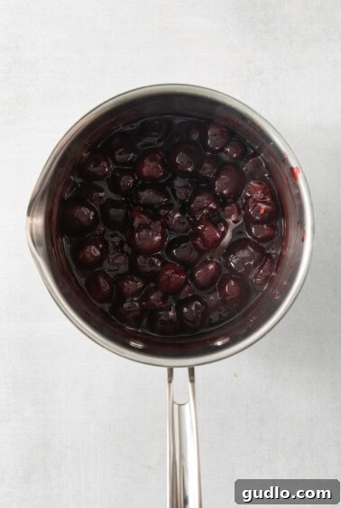 A saucepan filled with a vibrant cherry mixture simmering on a stovetop, ready to become a pie topping.