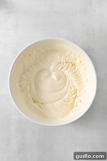 A white bowl filled with creamy, whipped frosting, showcasing the smooth and luxurious texture of the pie filling.
