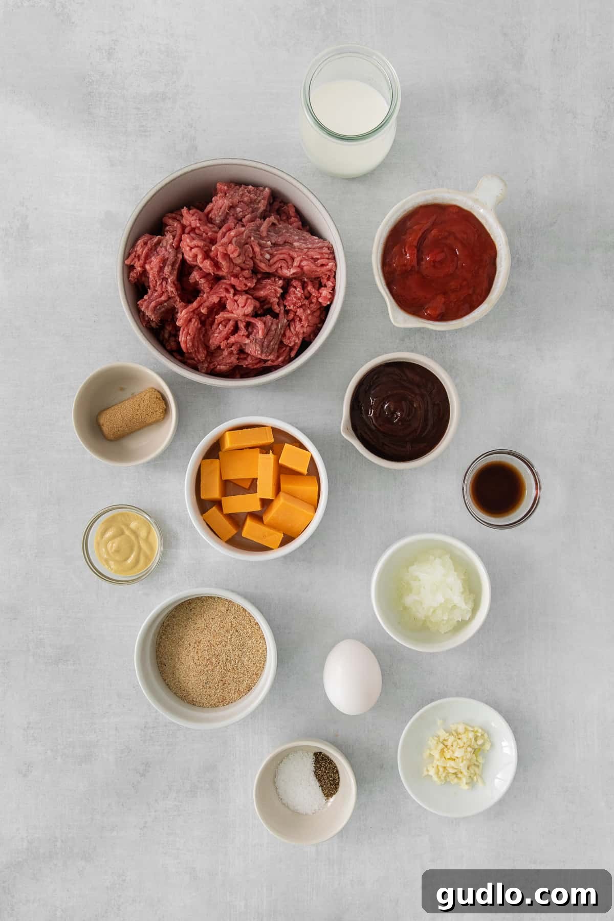 Individual Meatloaf Cups 3 Ingredients for ground beef burgers laid out on a grey background, including ground beef, spices, and sauces.