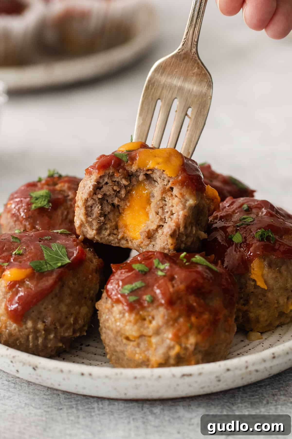 Individual Meatloaf Cups 9 One cheesy meatloaf muffin on a white plate with a fork, showing the melted cheese inside.