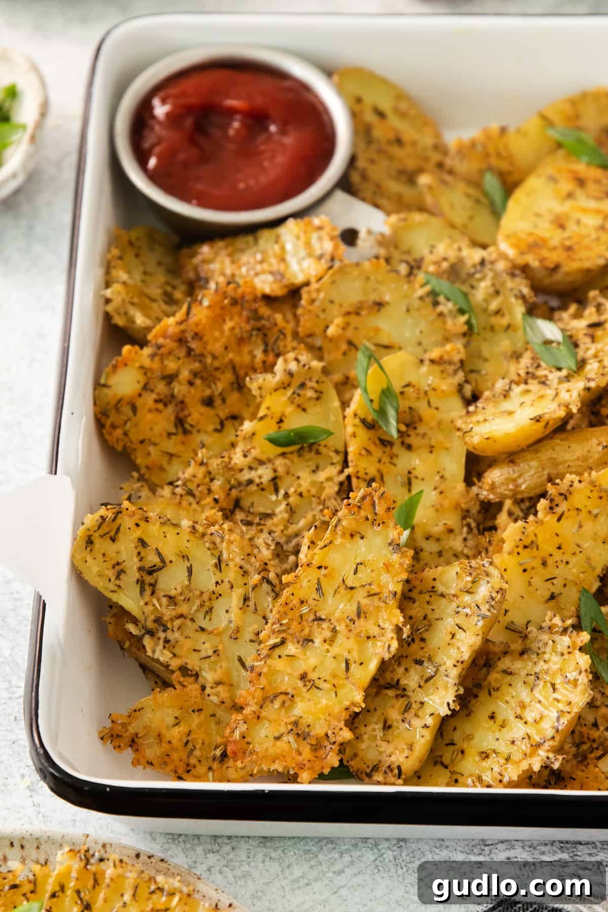 Golden Parmesan Potatoes 2 A tray of golden-brown crispy Parmesan crusted potato halves, ready to be served, with a small dish of ketchup on the side.
