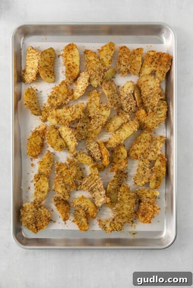 Golden Parmesan Potatoes 8 Crispy Parmesan crusted potato wedges being scooped from a baking sheet with a spatula, showing the golden cheese crust.