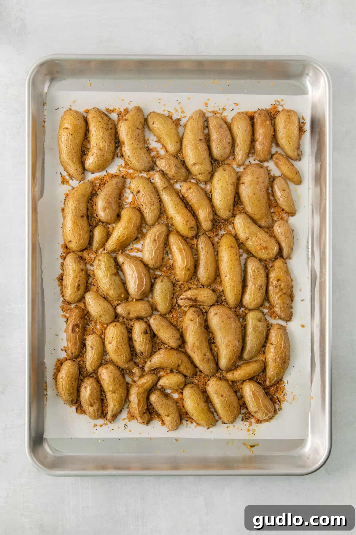 Golden Parmesan Potatoes 10 A baking sheet filled with freshly roasted Parmesan crusted potato halves, golden and glistening, with visible herb speckles.
