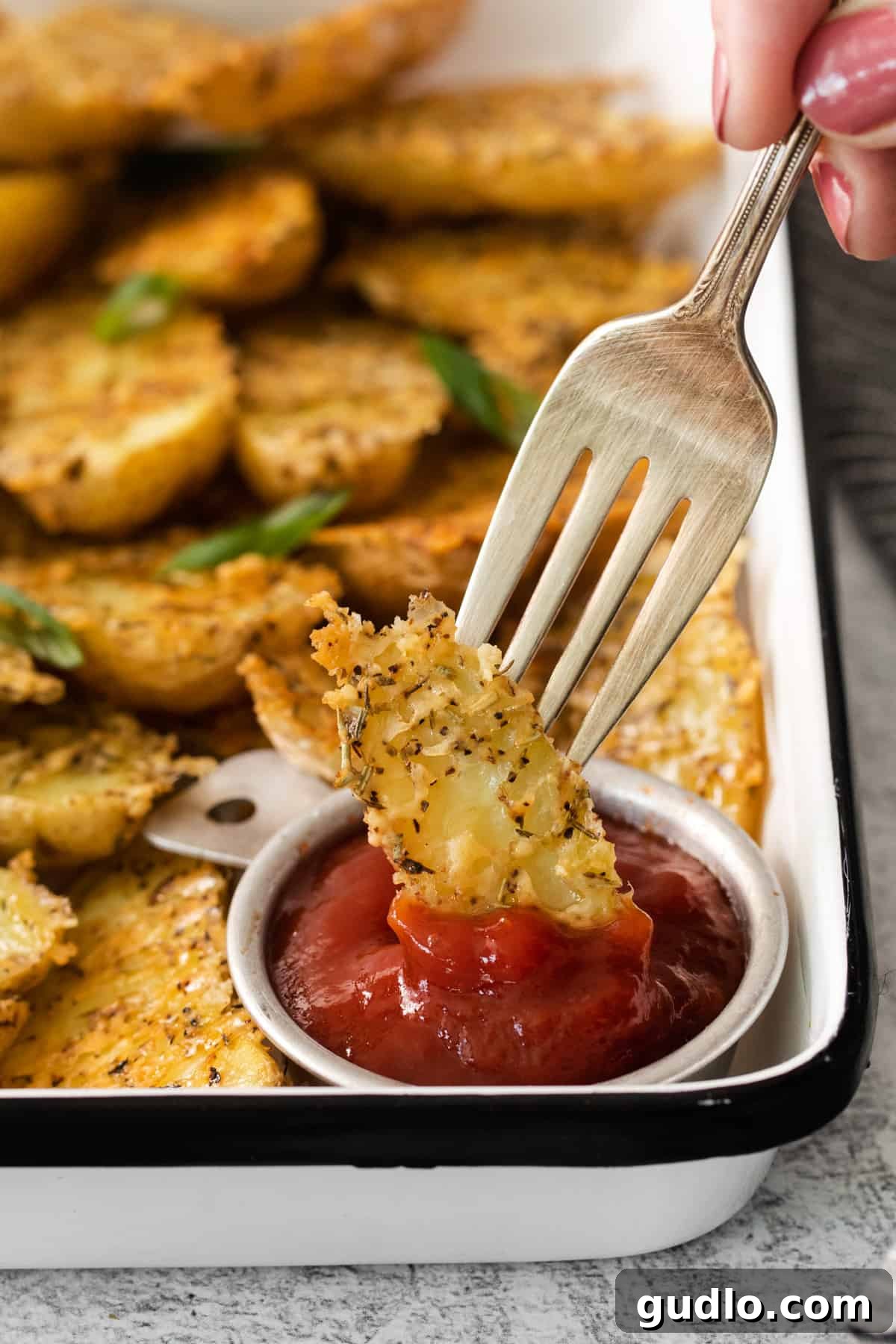 Golden Parmesan Potatoes 12 A person holding a fork over a serving tray of perfectly roasted Parmesan crusted potato wedges with a side of ketchup, highlighting their irresistible crispiness.