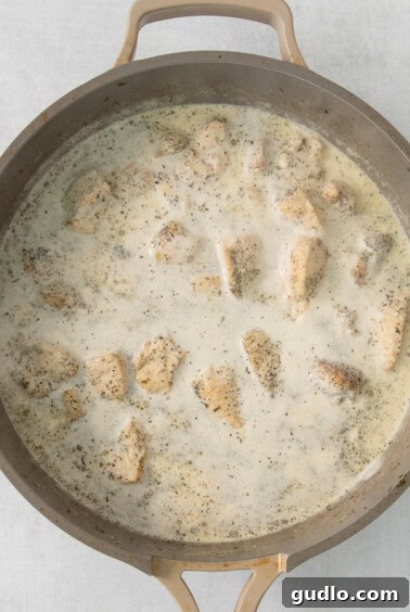 Chicken pieces simmering in a rich, creamy white sauce in a skillet.
