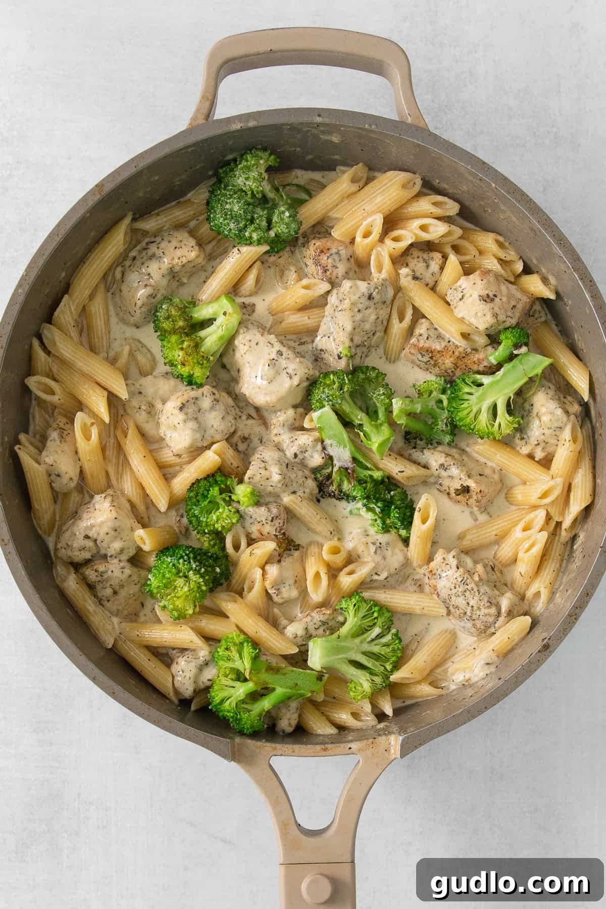 A vibrant skillet of chicken, broccoli, and penne pasta coated in a rich, creamy Alfredo sauce.