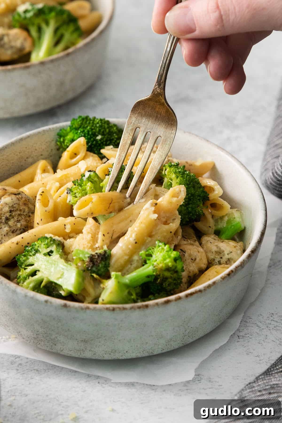 A person enjoying a forkful of creamy chicken broccoli alfredo from a bowl, highlighting its irresistible appeal.