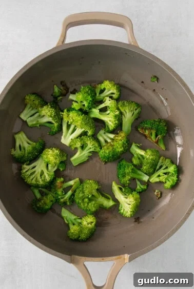 A pan filled with bright green sautéed broccoli florets on a stovetop.
