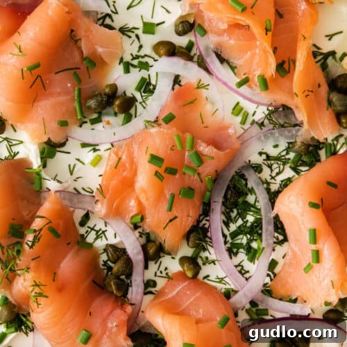 A close-up view of the finished cream cheese holiday board with smoked salmon, capers, onions, and dill, served with bagel pieces.