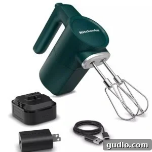 A green KitchenAid cordless hand mixer with various attachments.