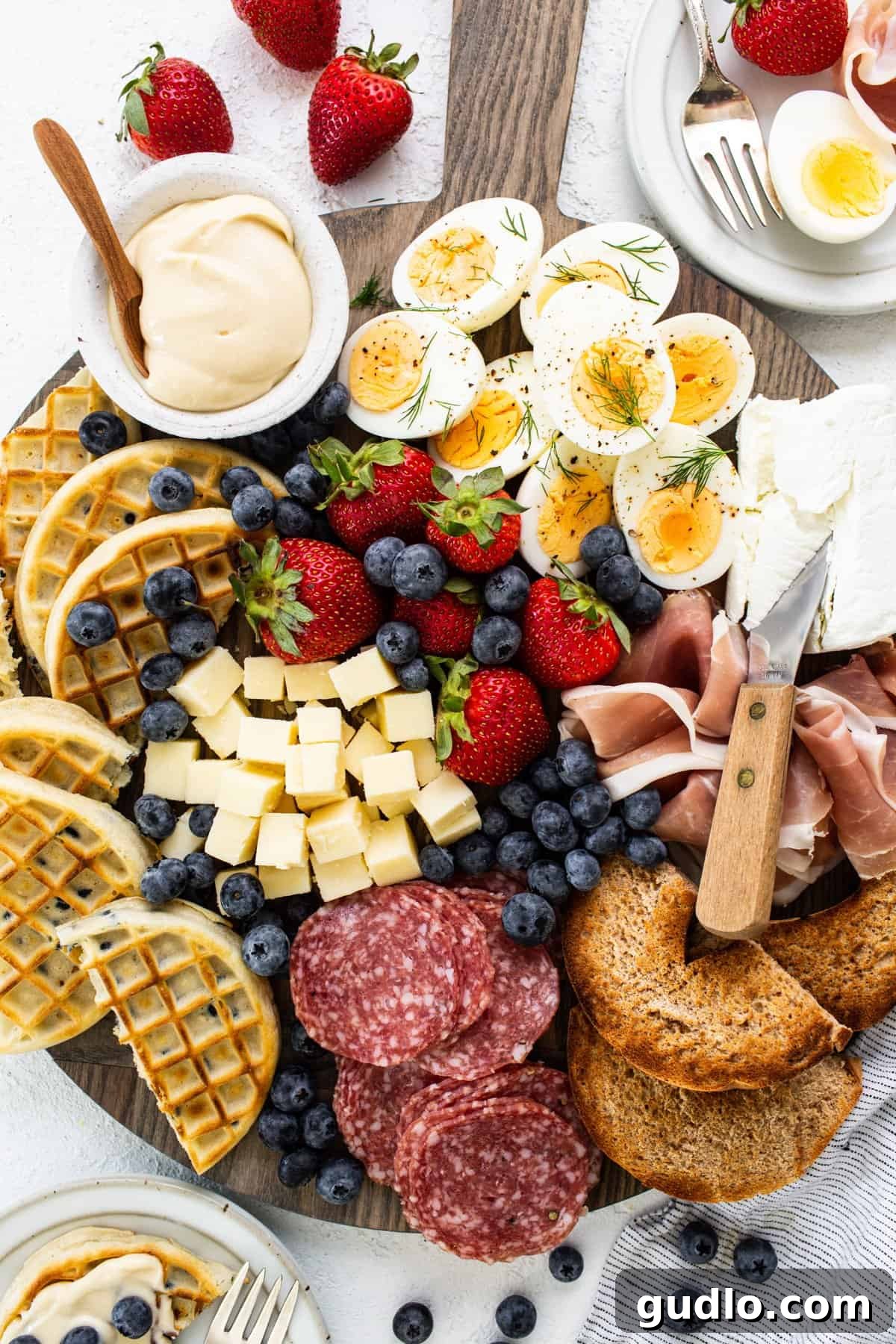 A beautifully arranged breakfast charcuterie board featuring a variety of meats, cheeses, fresh fruits, and golden waffles, inviting guests to indulge in a diverse morning spread.