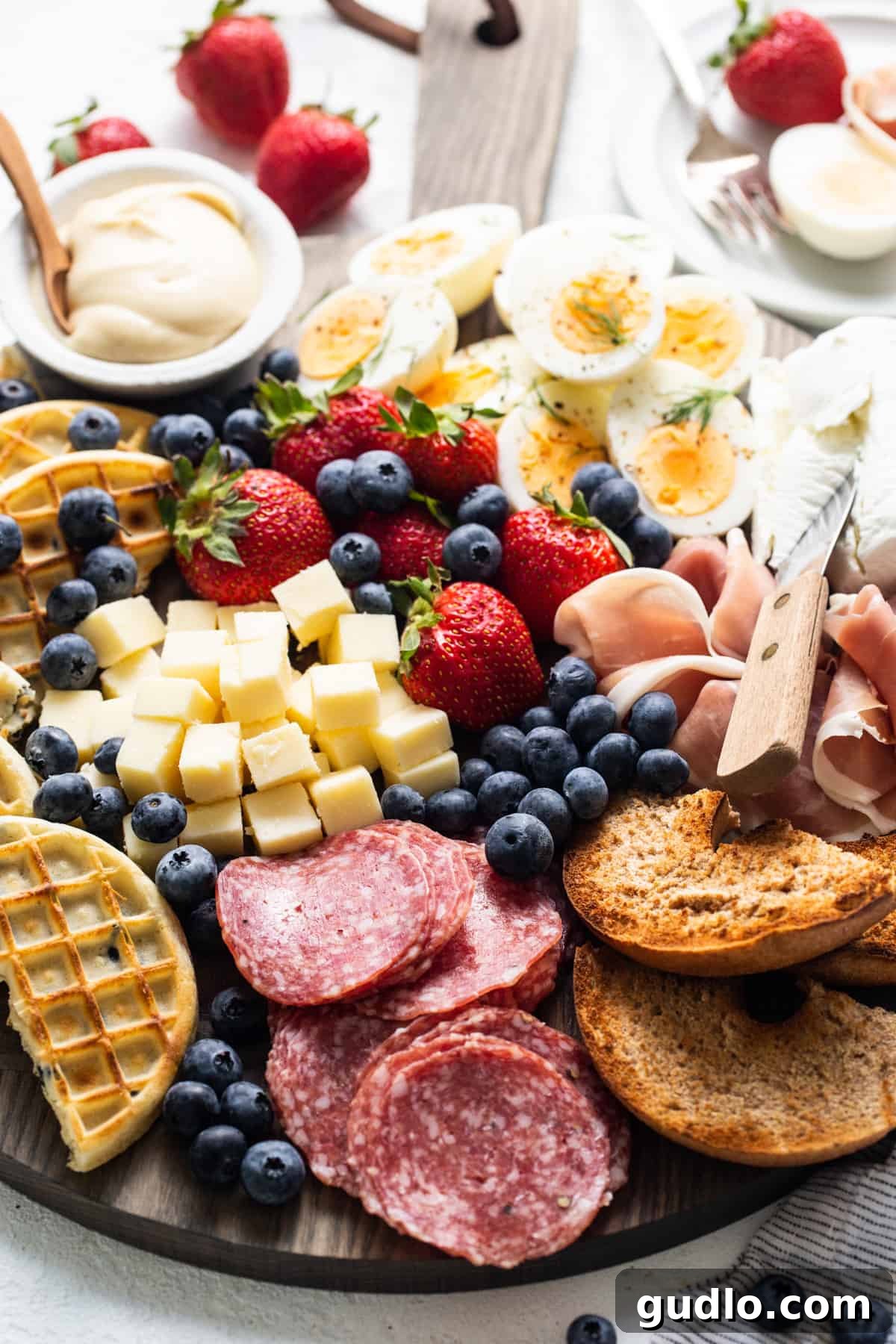 An elaborate breakfast charcuterie board, fully loaded with an assortment of meats, cheeses, fresh fruits, and toasted waffles, ready for serving and enjoyment.