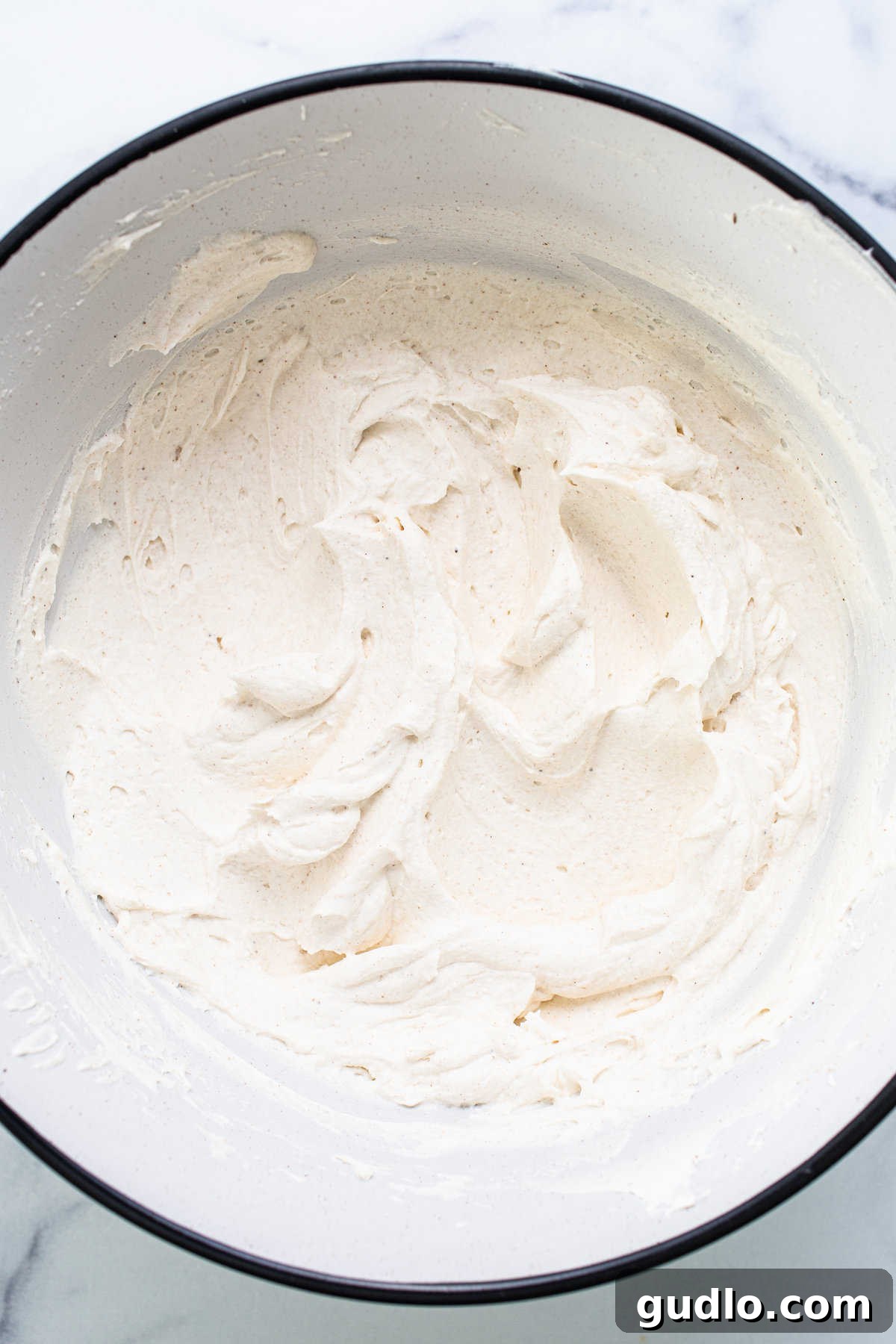 Freshly whipped mascarpone cream in a large bowl, ready for layering, set against a marble countertop.