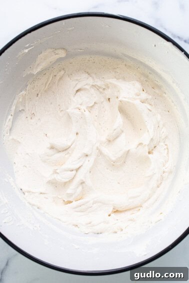 Whipped mascarpone cream in a bowl, showing soft peaks, on a marble countertop.