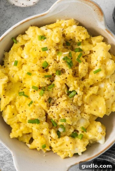 Scrambled eggs in a bowl with chives and sour cream.