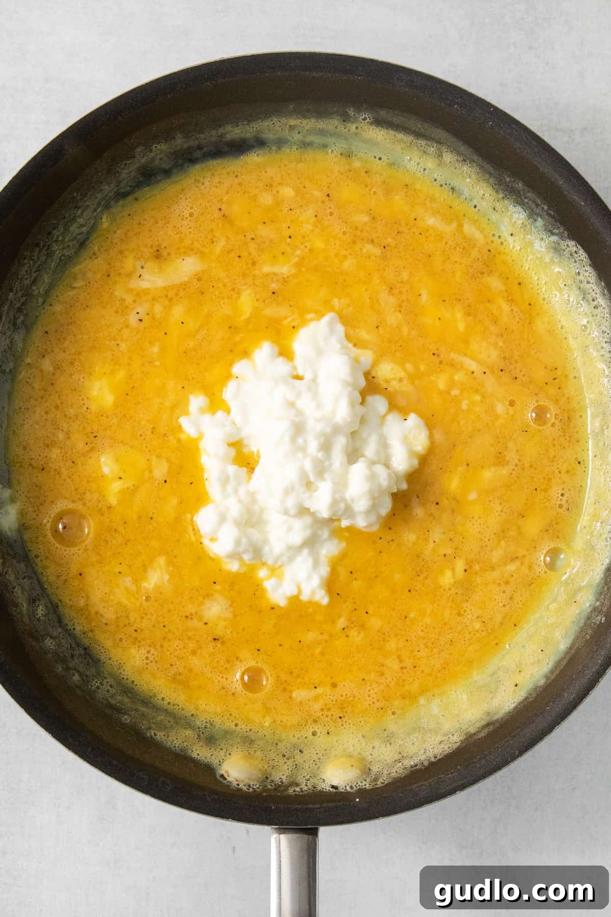A frying pan with a yellow sauce and feta cheese.