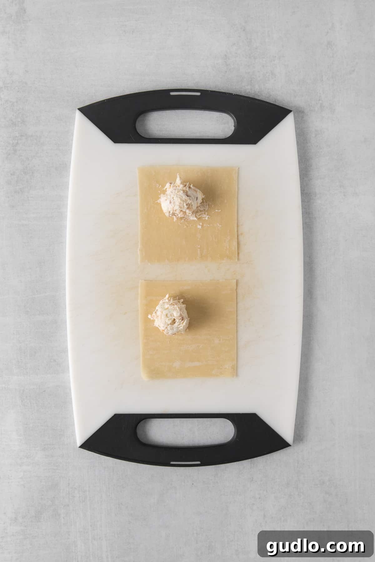 Crispy Air-Fried Crab Rangoons 3 A cutting board with two pieces of wonton wrappers, one being filled with crab mixture.