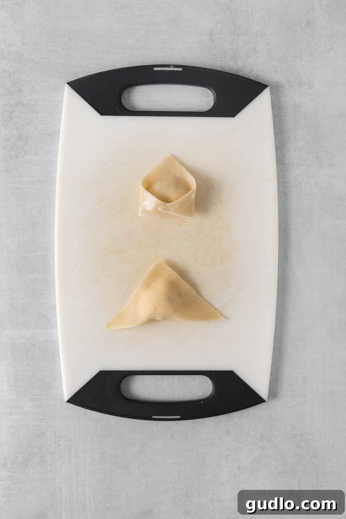 Crispy Air-Fried Crab Rangoons 4 A cutting board showing two neatly folded dumplings, ready for cooking.