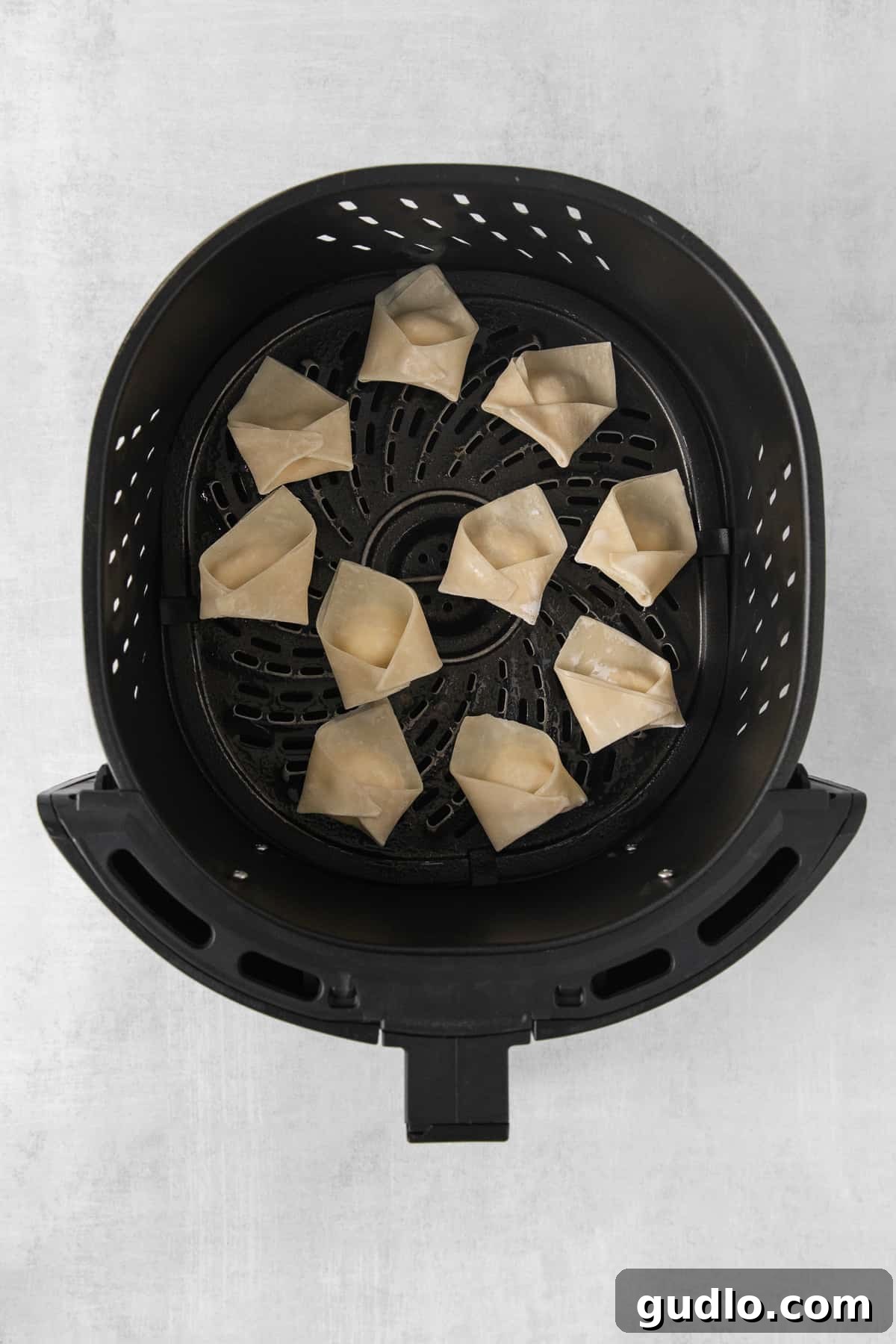 Crispy Air-Fried Crab Rangoons 5 An air fryer basket filled with partially cooked fried dumplings.