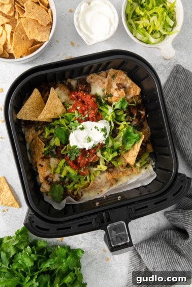 No-Fuss Air Fryer Nachos 12 A close-up view inside an air fryer, filled with a vibrant heap of nachos, some drizzled with sour cream.