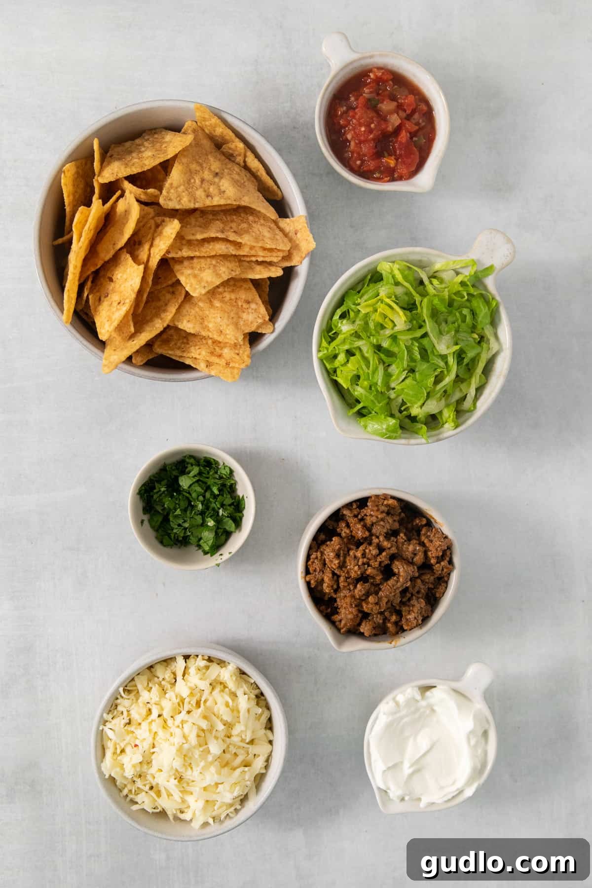 No-Fuss Air Fryer Nachos 3 Various bowls of vibrant tortilla chips, fresh salsa, creamy sour cream, and rich guacamole, ready to top a nacho platter.