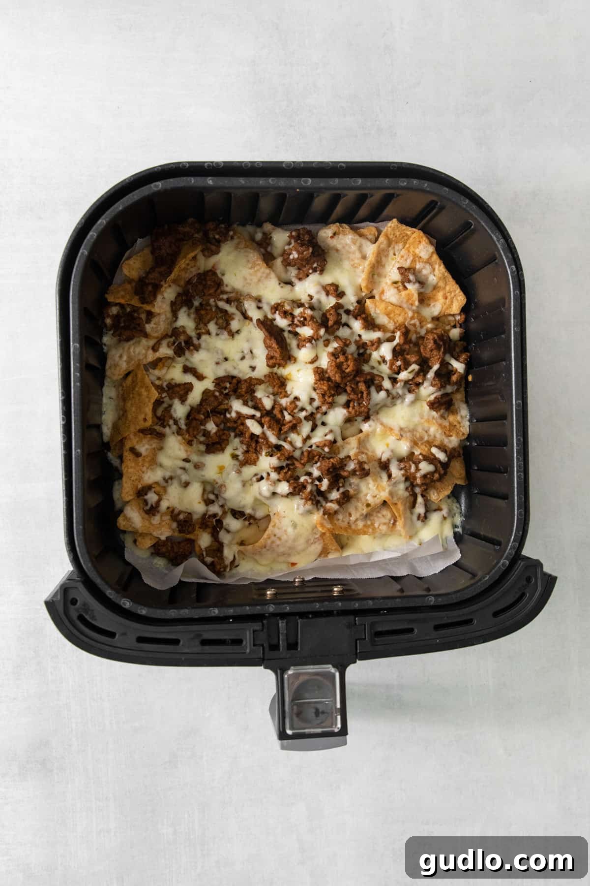 No-Fuss Air Fryer Nachos 5 An air fryer basket filled to the brim with bubbly, golden, cheesy nachos, straight out of the appliance.