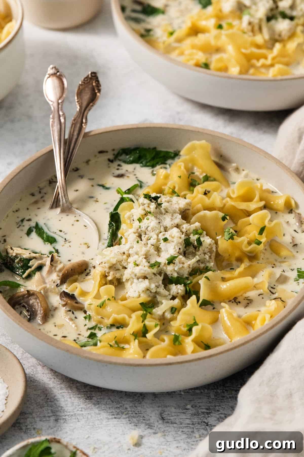 Hearty Cream Lasagna Soup 4 Two bowls of creamy white lasagna soup, garnished with fresh spinach and herbs.