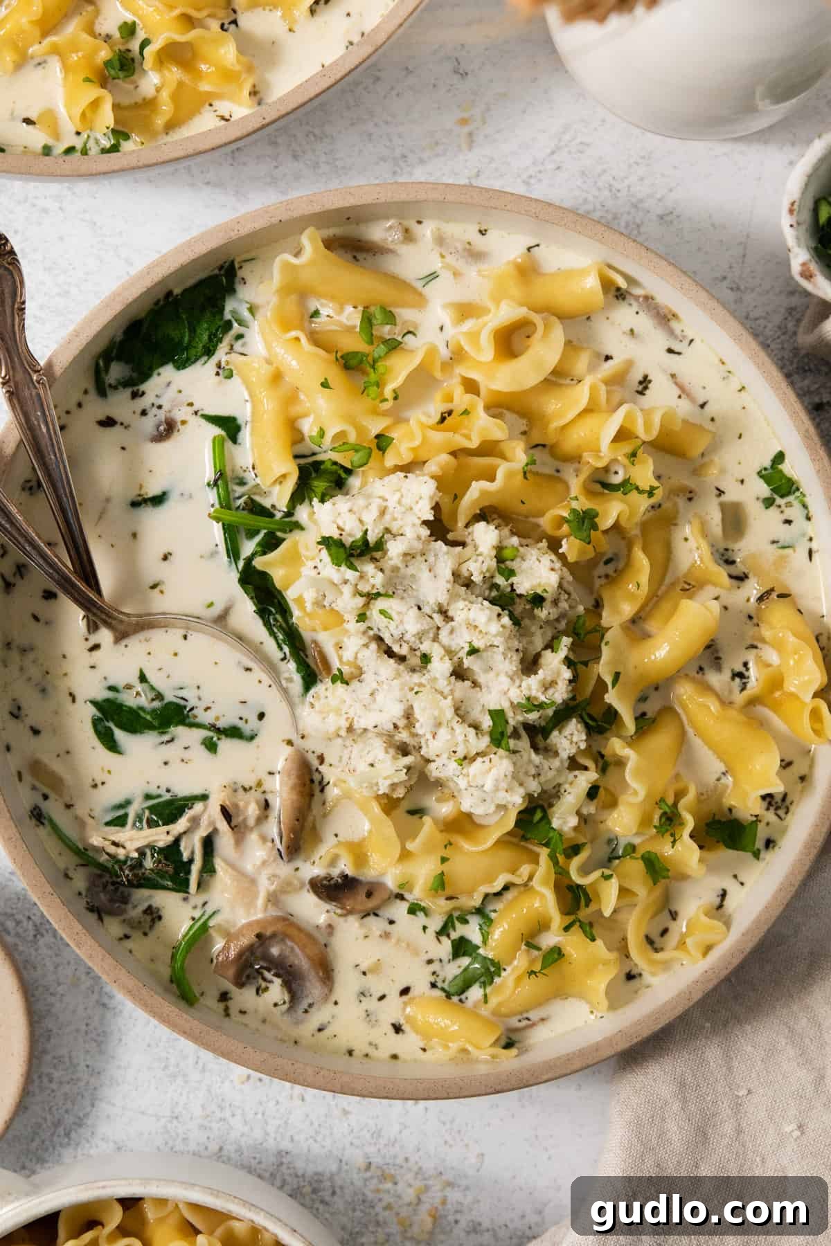 Hearty Cream Lasagna Soup 5 A close-up of a bowl of creamy mushroom and spinach soup with a spoon, ready to eat.