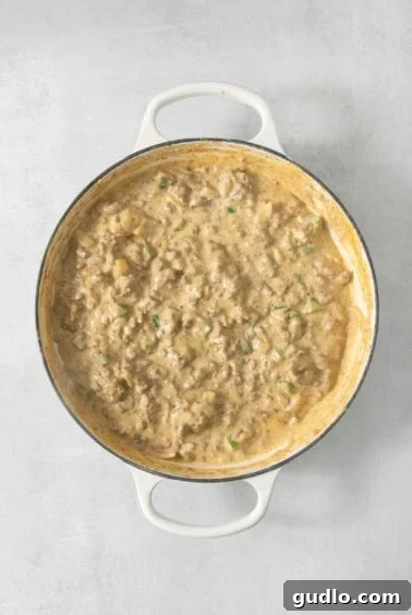 Decadent Philly Cheesesteak Dip 10 Cream cheese and Velveeta melting into the beef mixture in a pan.