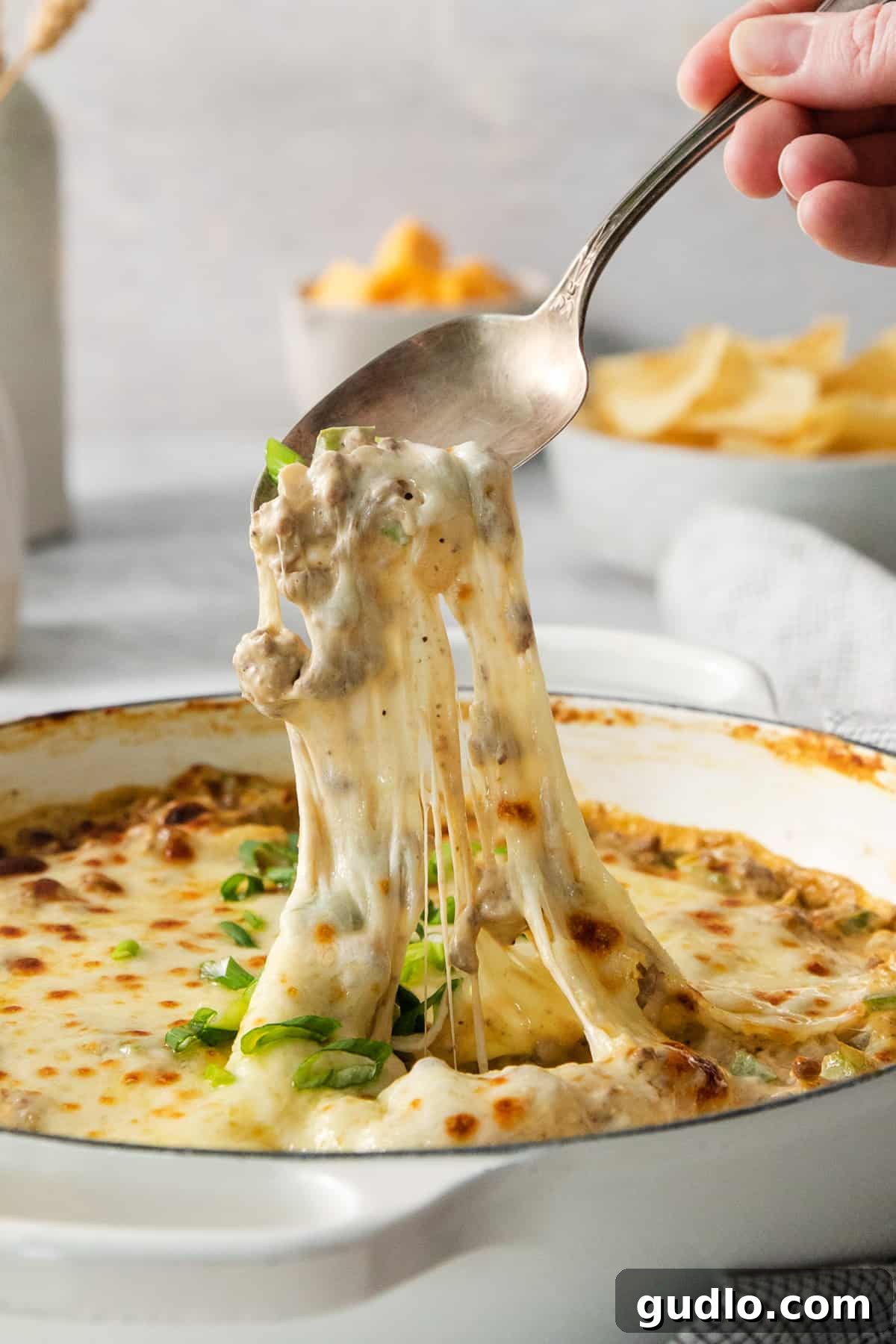 Decadent Philly Cheesesteak Dip 6 A serving spoon lifting a spoonful of hot, gooey Philly Cheesesteak Dip from a casserole dish.