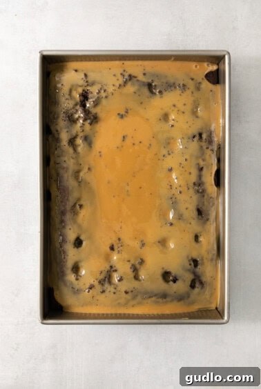 Ultimate Indulgence Cake 14 Chocolate cake in a pan with caramel sauce drizzled over it, soaking into the poked holes.