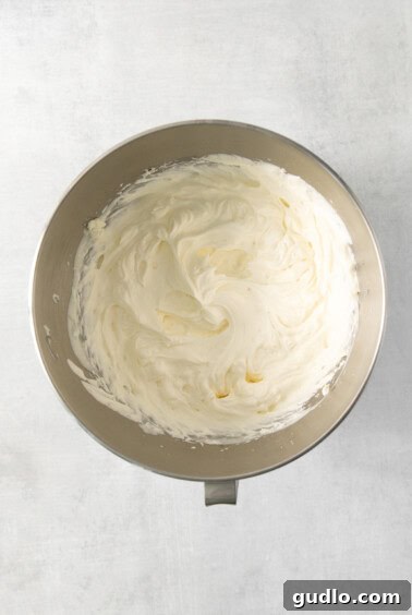 Ultimate Indulgence Cake 15 Fluffy cream cheese frosting being whipped to perfection in a metal mixing bowl.