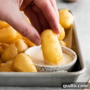 Golden Homemade Corndog Bites 4 A person dipping a dipping sauce into a tray of french fries.