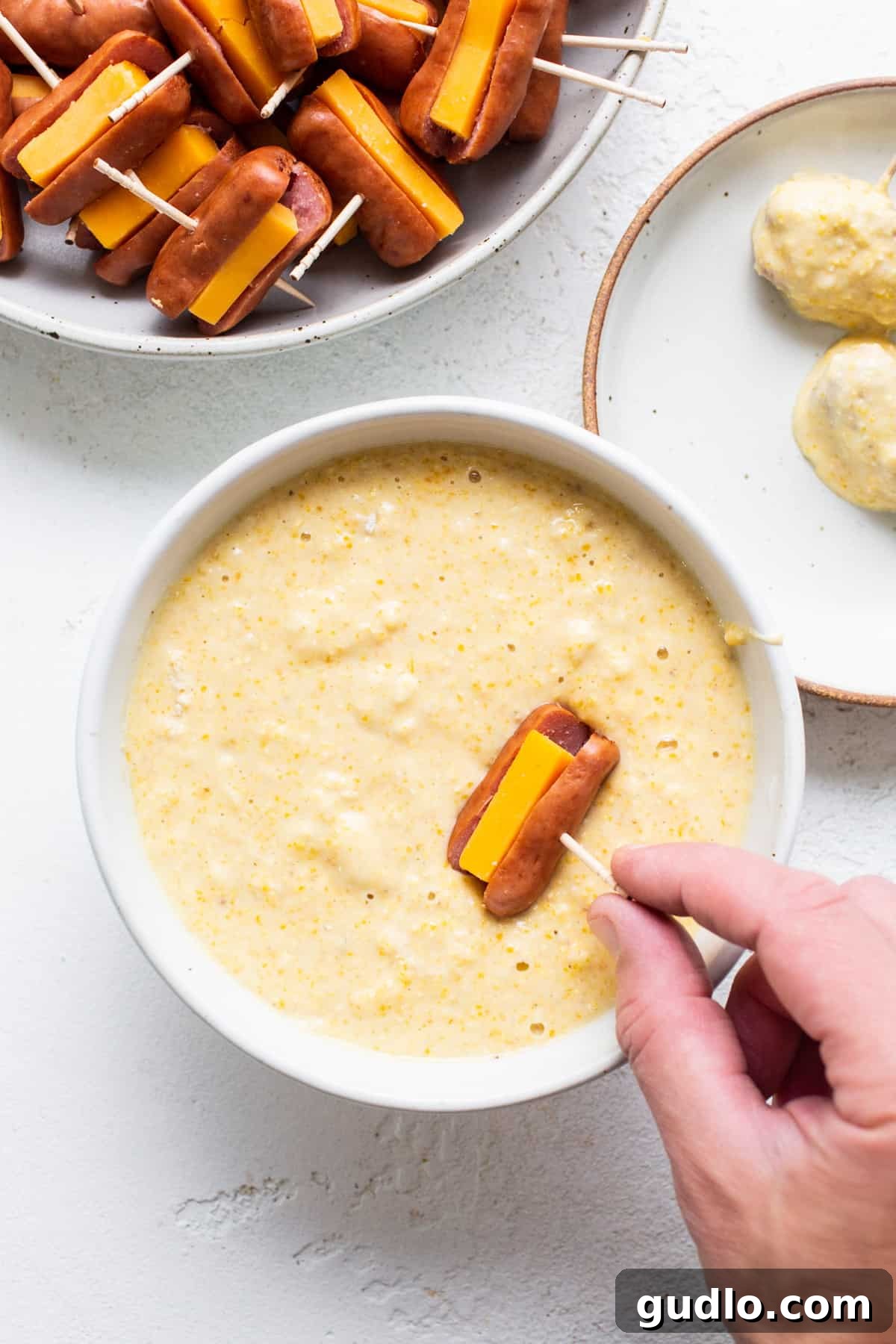 Golden Homemade Corndog Bites 5 A person is dipping a mini corndog into a bowl of batter.