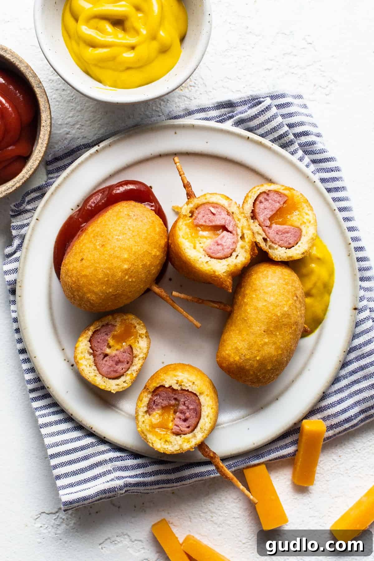 Golden Homemade Corndog Bites 7 A single mini corndog on a stick with ketchup and cheese on a plate.