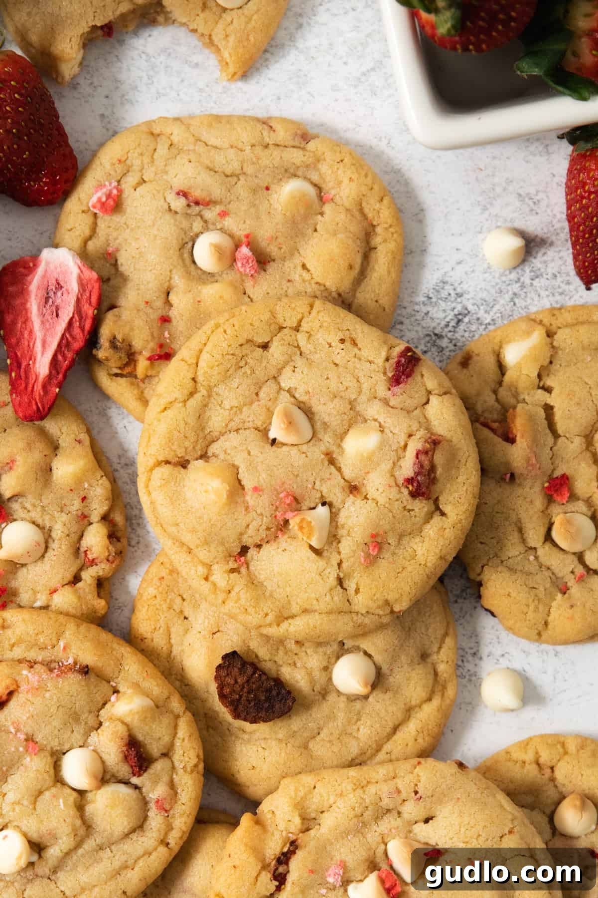 A pile of perfectly baked strawberry cheesecake cookies adorned with fresh strawberries and white chocolate chips.