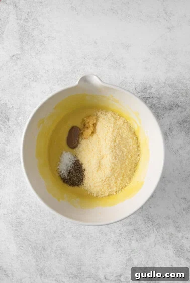 A white bowl filled with all the savory Caesar dressing ingredients including cheese, anchovy paste, and spices, ready for a final blend.
