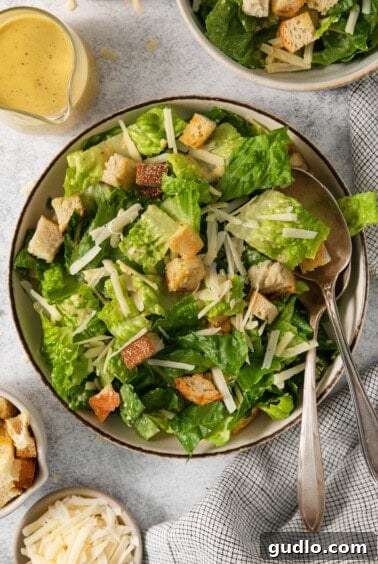 A final close-up of the fully dressed Caesar salad in a white bowl, showing the rich coating of dressing on the fresh lettuce and crispy croutons.