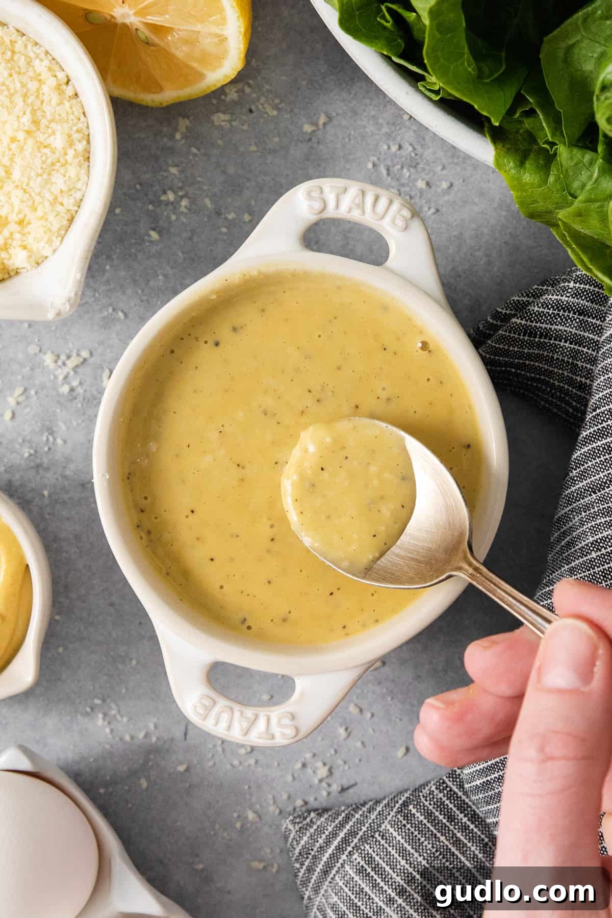 A person meticulously pouring the creamy, golden Caesar dressing into a mixing bowl, showcasing the dressing's smooth consistency.