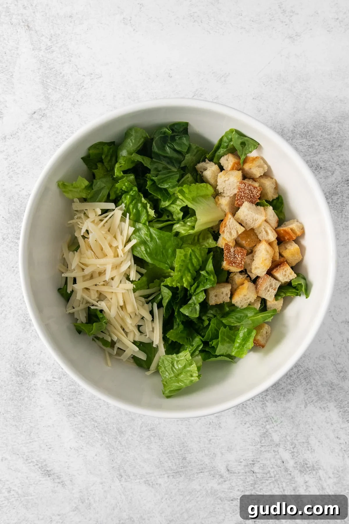 A pristine white bowl filled with a fresh Caesar salad, showcasing perfectly chopped romaine, abundant golden croutons, and generous shavings of Parmesan cheese.