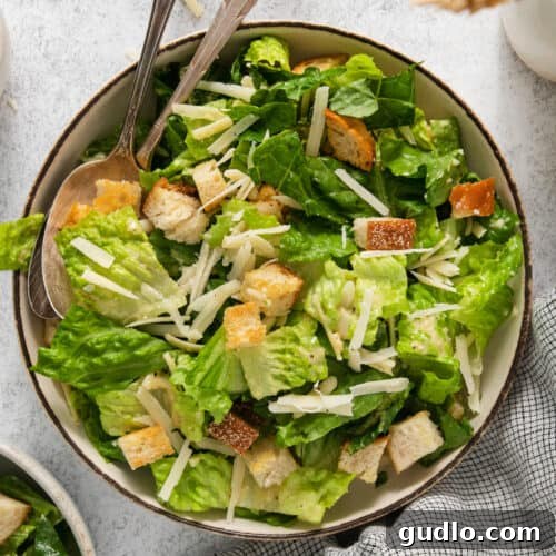A beautifully arranged bowl of classic Caesar salad, showcasing crispy romaine, golden croutons, and generous Parmesan shavings, ready to be served.