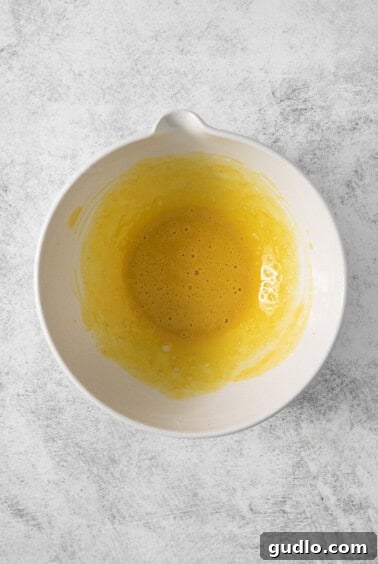 A white bowl with the initial frothy mixture of egg yolk, Dijon mustard, and lemon juice, perfectly prepared for the next step.