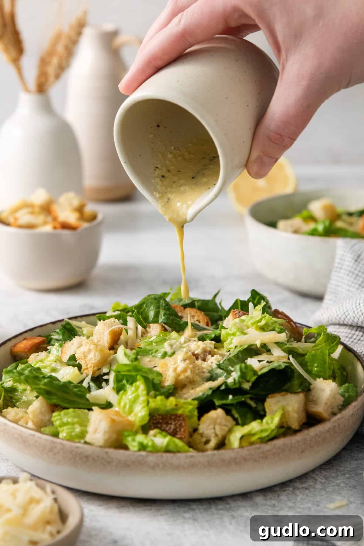 Classic Caesar Dressing 2 A person pouring homemade Caesar dressing onto a crisp Caesar salad.