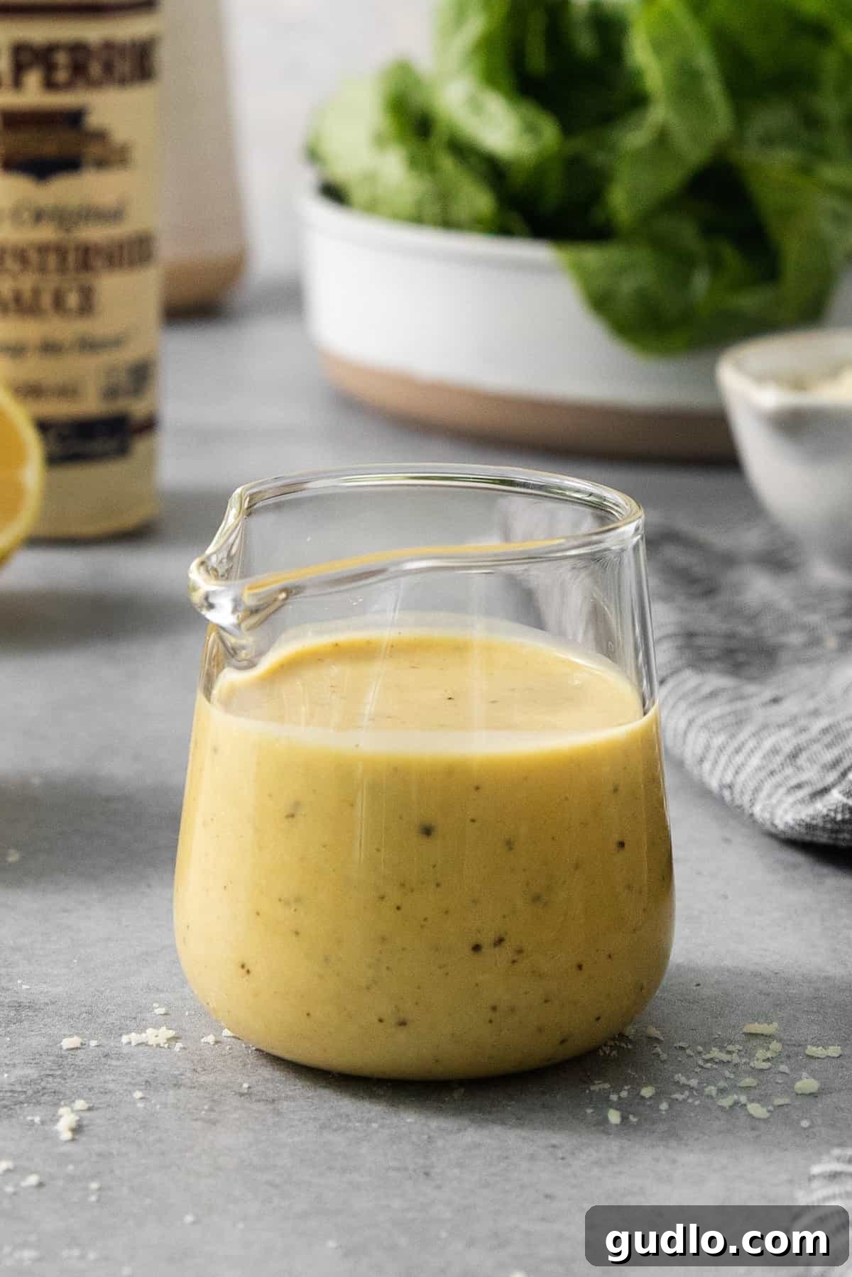 Classic Caesar Dressing 4 A bowl of creamy Caesar dressing sits on a table next to a bottle of fresh lemon juice, ready to be seasoned.