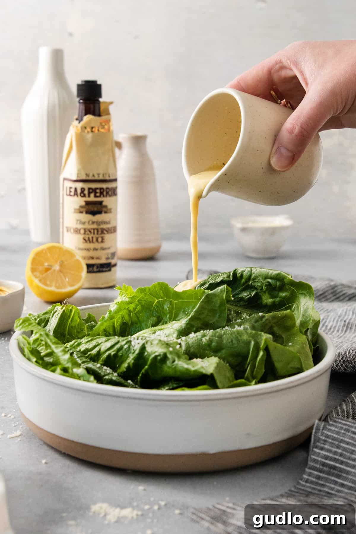 Classic Caesar Dressing 7 A person pouring a generous amount of homemade Caesar dressing over a fresh Caesar salad.