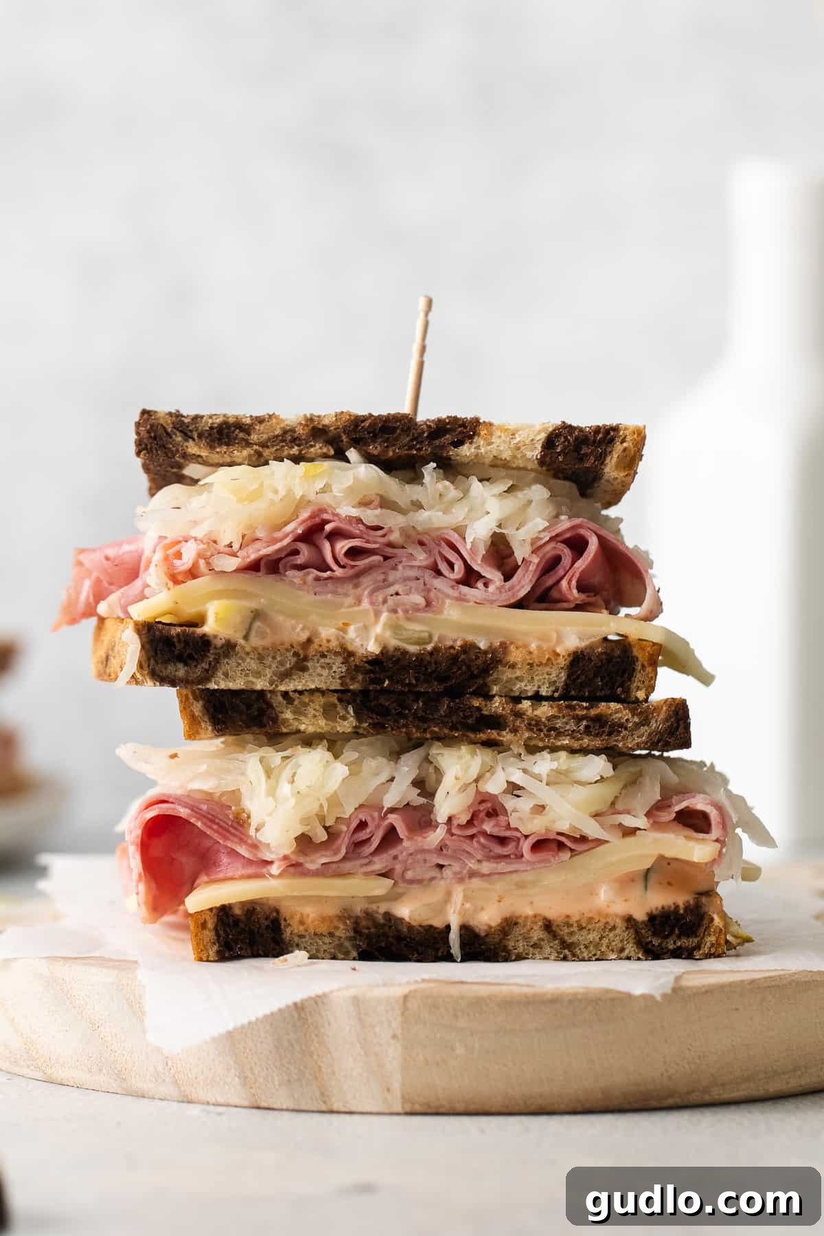 A perfectly assembled Reuben sandwich on a wooden cutting board, showcasing layers of corned beef, Swiss cheese, sauerkraut, and dressing between marbled rye bread.
