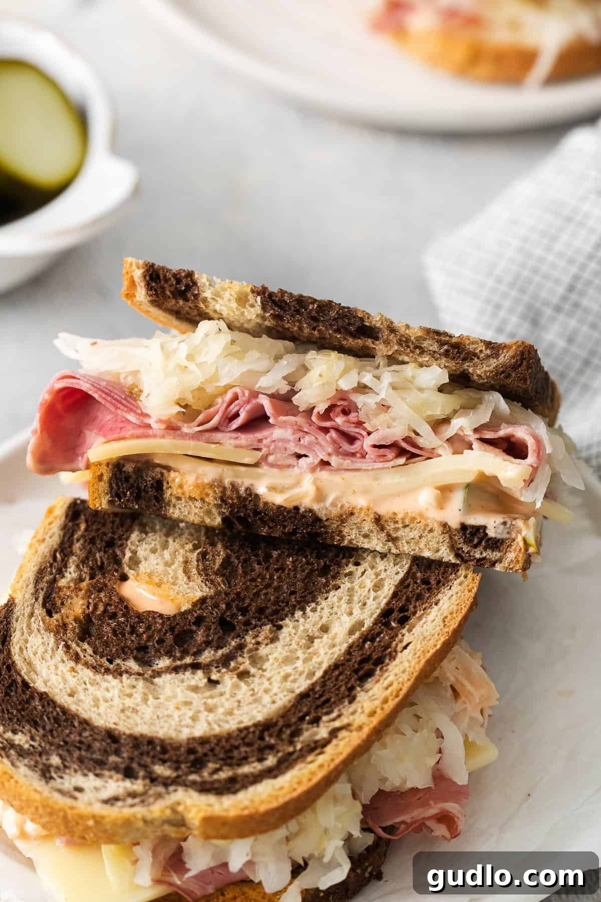 A half-eaten Reuben sandwich on a plate with a side of chips, showing the rich layers of filling.